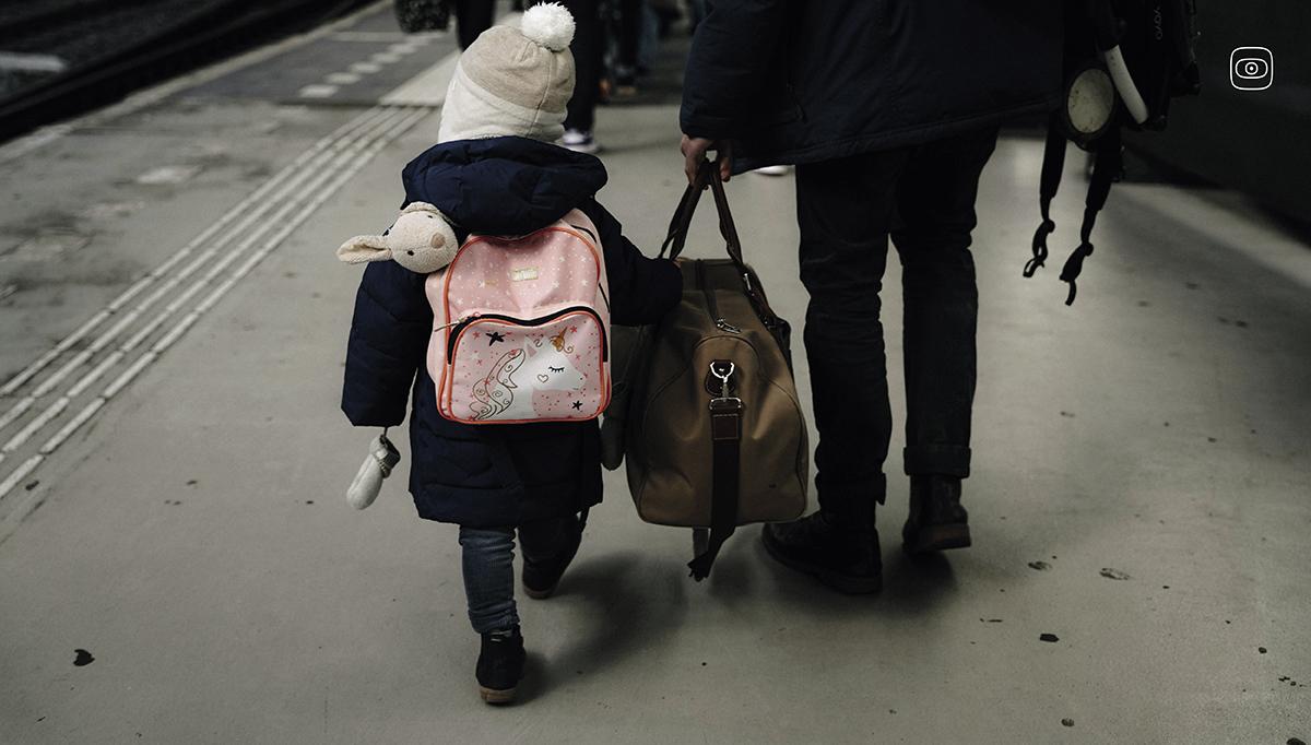 A child walking on a train platform with a guardian. 