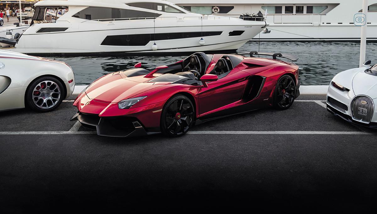 A red supercar with an open-top design is parked at a marina.