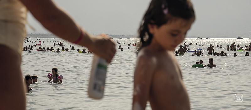 Beachgoers lather on sunscreen while bathing along the Mediterranean shoreline in Palermo, Sicily