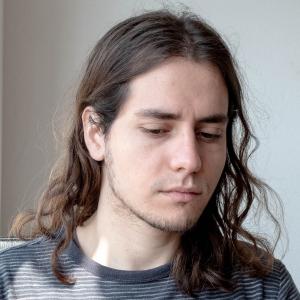 Jordi Jon - a young man with dark shoulder-length hair, not looking directly into the camera